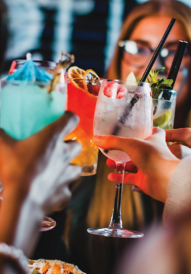 A close-up image of 4 colourful cocktails brought together in a "cheers" motion